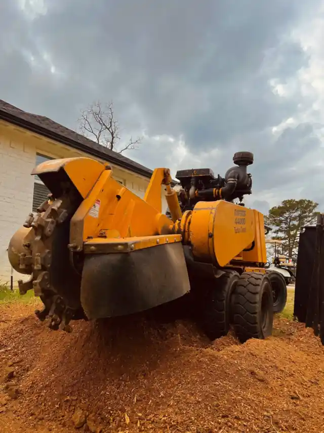 A stump grinder throwing red East Texas soil under a storm sky